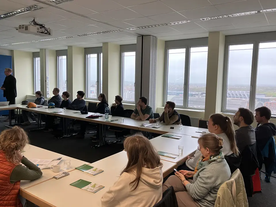 Die G&auml;ste aus N&uuml;rnberg sitzen hufeisenf&ouml;rmig in einem Besprechungsraum und h&ouml;ren einem Vortrag zu.