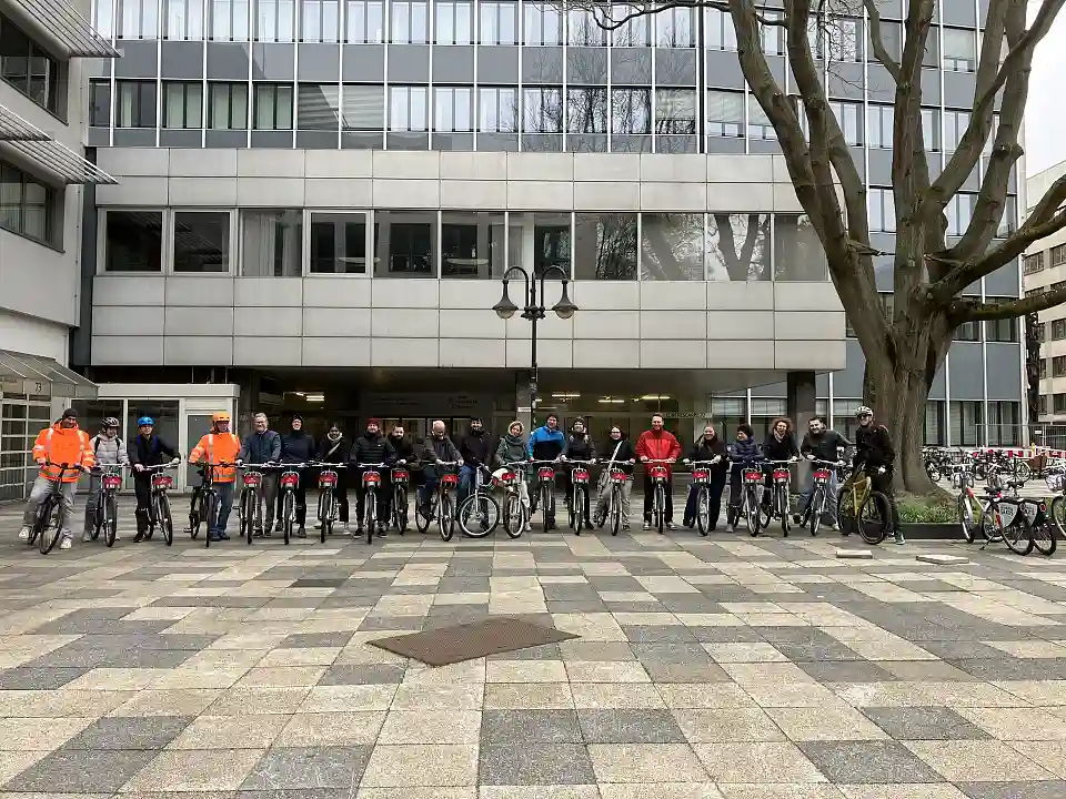 Gruppenbild vor dem SBMS-Geb&auml;ude - zu sehen sind Personen mit Fahrr&auml;dern im Halbkreis.