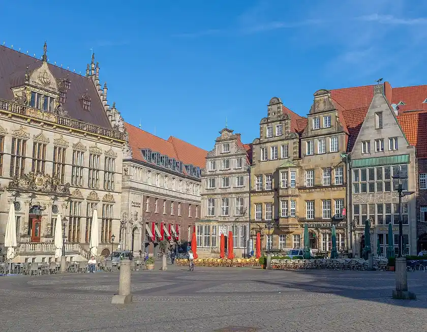 Blick auf den Bremer Marktplatz mit seinen historischen Gebäuden vor blauem Himmel. Vor den Gebäuden viele Tische, Stühle und Sonnenschirme
