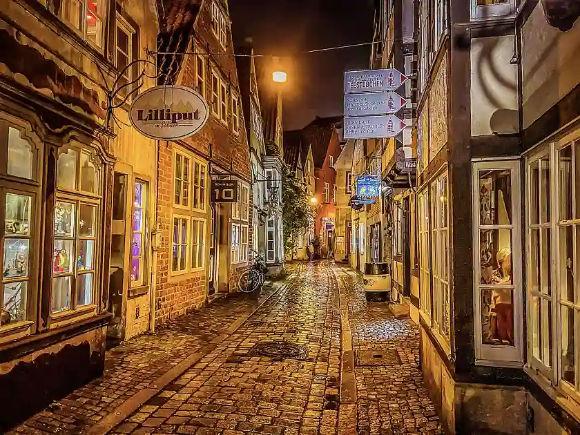 Das Schnoorviertel bei Nacht. Eine schmale Kopfsteinpflastergasse mit alten, kleinen Häuschen links und rechts im Schein einer warmen, gelblichen Straßenbeleuchtung. 