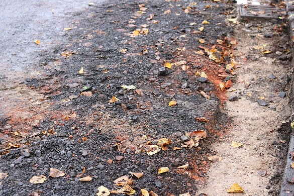 Offengelegte Tragschicht einer Straße mit roten Spuren, die auf Schutt aus dem zweiten Weltkrieg hinweist. Auf der Schicht liegen mehrere Laubblätter
