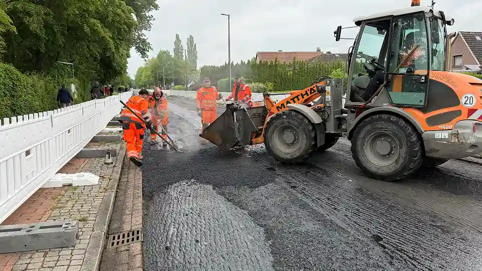 Zu sehen sind Stra&szlig;enbauarbeiten. Die Fahrbahndecke wird unter Absperrungen erneuert.