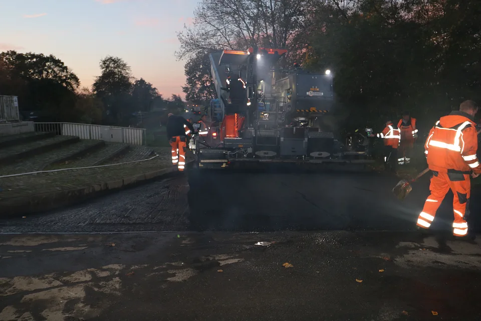 Anfangs wird der hei&szlig;e Asphalt noch per Schaufel verteilt, bevor die R&uuml;ttelbohle dies &uuml;bernimmt.