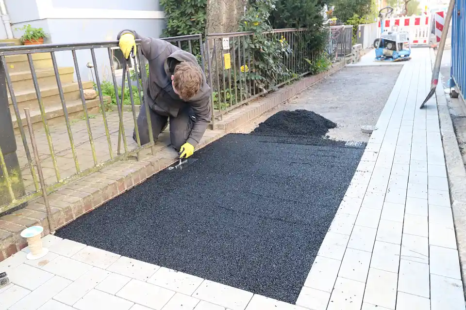 Ein Teilst&uuml;ck eines Weges mit frischem, feuchten Bodenbelag. Nach dem Einguss wird das Material mit der Kelle von einem blonden Mann verteilt und angedr&uuml;ckt.