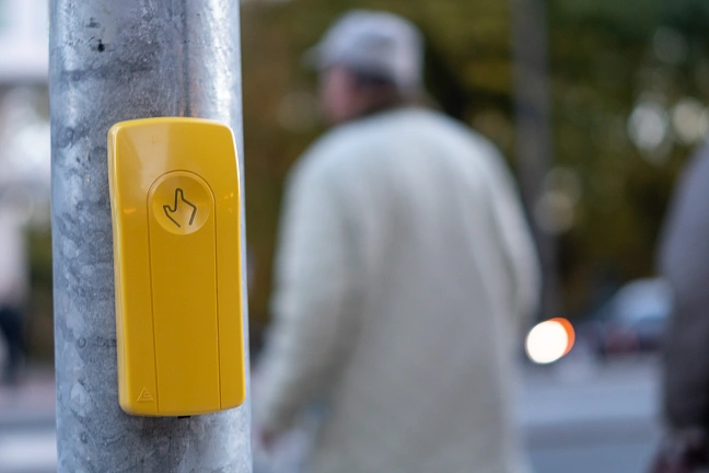Ein älterer Herr steht neben einer Ampel, die per Schalter bedient werden kann.